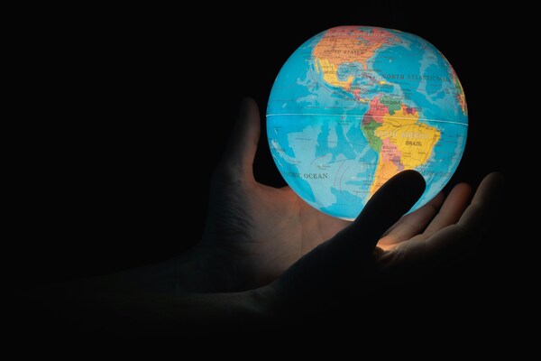 Un mundo, con américa latina de frente, sostenido por unas manos masculinas