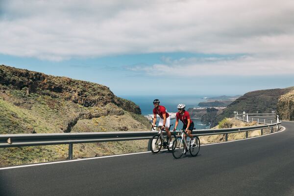 Dos ciclistas vestidos de rojo, hombre y mujer, recorriendo una carretera